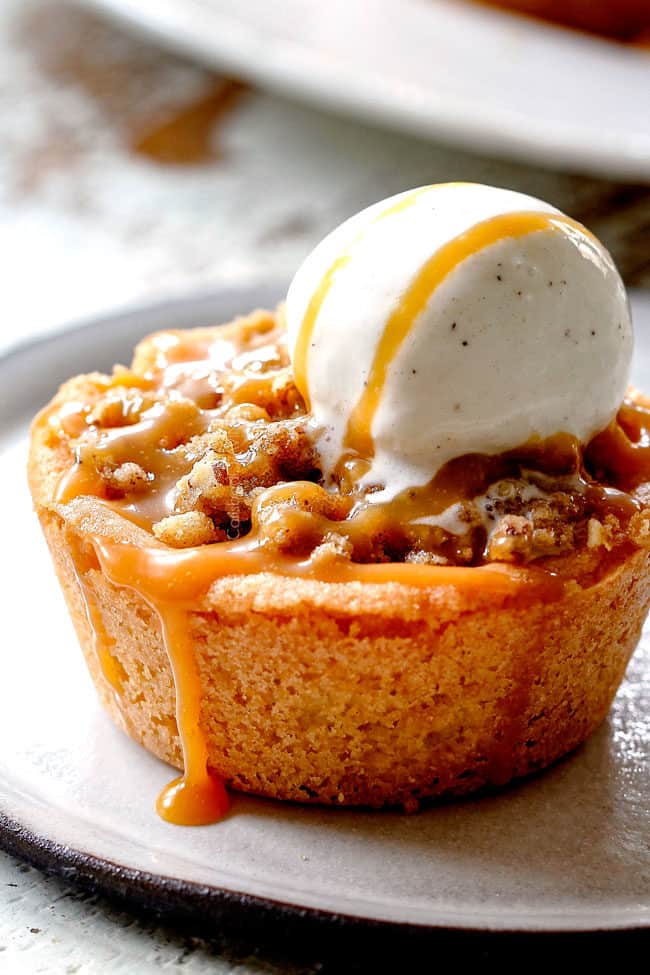 up close of caramel apple pie with streusel topping with ice cream and caramel dripping down the side