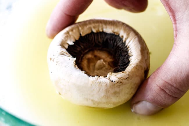showing how to make sausage stuffed mushrooms by dipping mushrooms in butter before baking