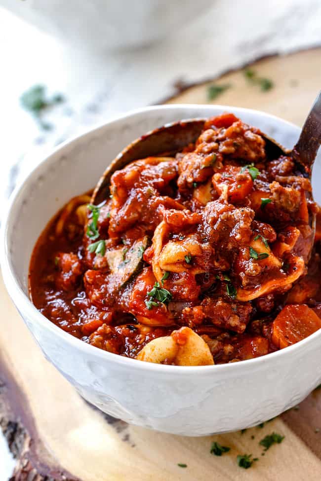 pouring a ladle of sausage tortellini soup into a white bowl with a silver ladle.