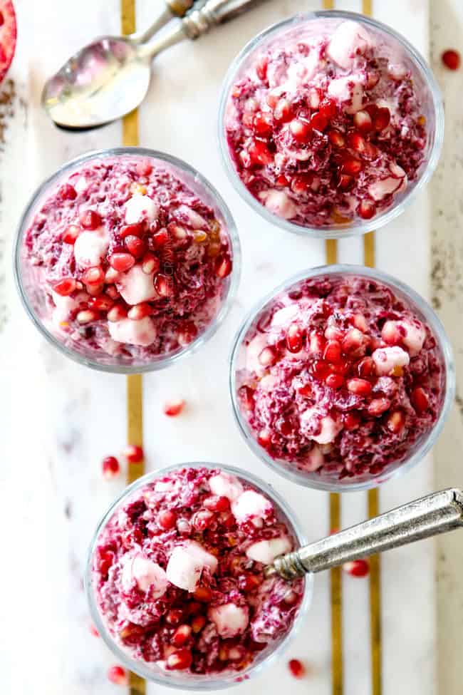 top view of creamy ambrosia salad with pineapple, mandarin oranges, mini marshmallows, cranberries and pomegranate seeds with creamy dressing with yogurt in small glass serving dishes