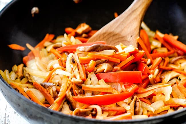 showing how to make Korean Noodles by stir-frying shiitake mushrooms, onions, carrots in a skillet