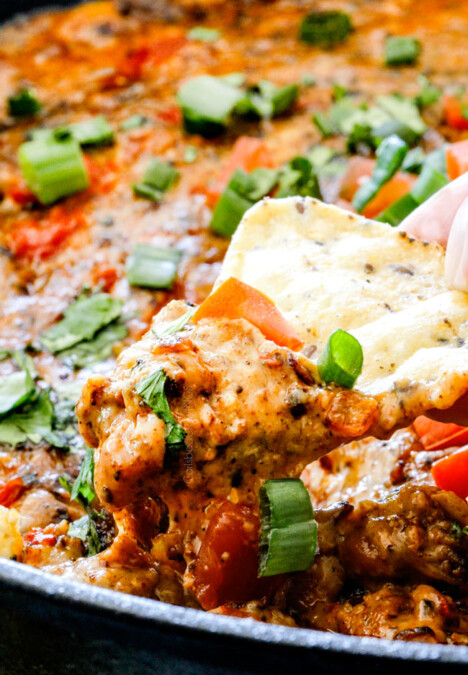 up close of a tortilla chip dipping into Queso Fundido with gooey melty cheese