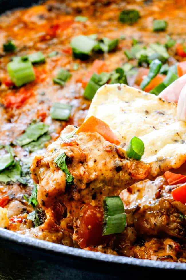 up close of a tortilla chip dipping into Queso Fundido with gooey melty cheese