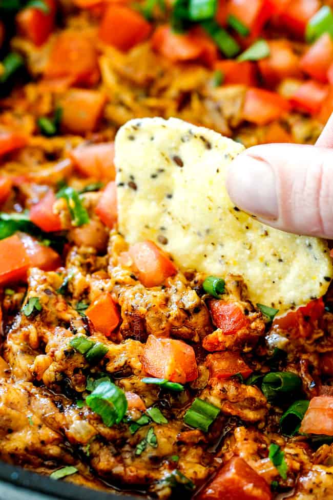 up close of a tortilla chip dipping into spicy Chorizo Queso