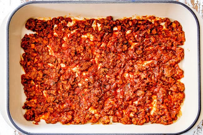 showing how to layer lasagna with a layer of meat sauce on the bottom of the pan