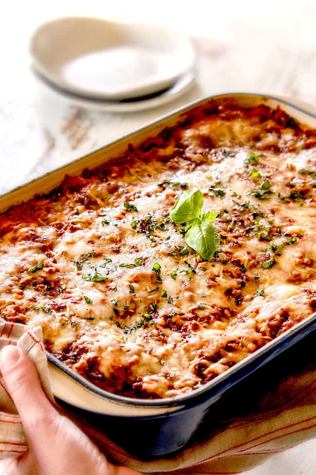 two hands holding a pan of traditional lasagna in a blue dish