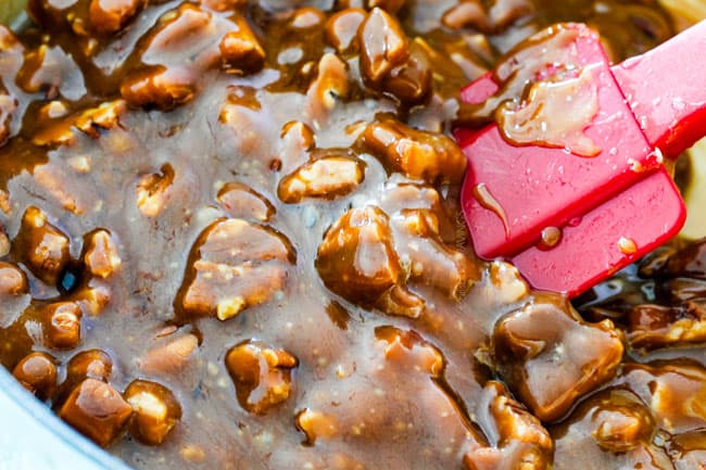 showing how to make pecan topping for Pecan Pie Cheesecake by stirring pecans into caramel