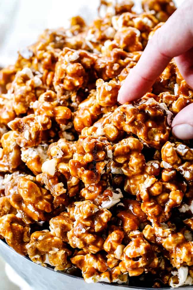 two fingers taking a piece of caramel popcorn from a large bowl