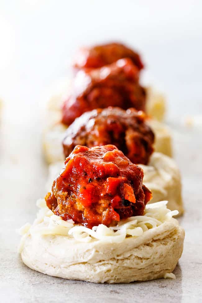 showing how to make pull apart bread by adding meatballs and cheese to biscuits