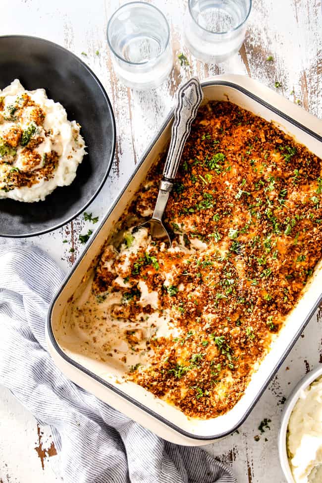 top view of chicken divan from scratch in a blue casserole dish with a silver spoon and some of the casserole gone with mashed potatoes on the side