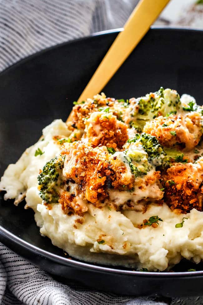 up close of a serving of chicken divan with broccoli and chicken with mashed potatoes in a black bowl with a gold fork