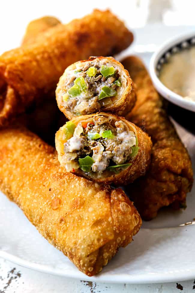Philly Cheesesteak Egg Rolls Recipe on blue and white serving plates with a side of queso