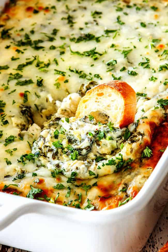 up close of a piece of bread dipped into spinach and artichoke dip