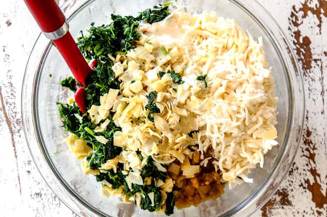 top view of showing how to make hot spinach artichoke dip recipe by adding spinach, artichokes, cream cheese, sour cream, mayonnaise, mozzarella and Parmesan cheese to a glass bowl