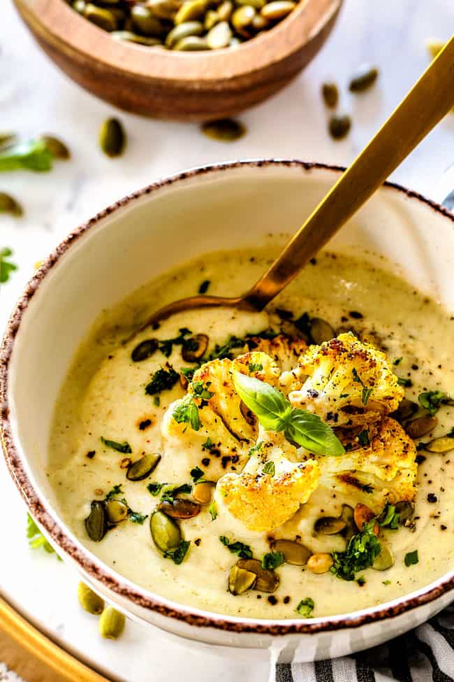 side view of healthy cauliflower soup with a golden spoon and freshly cracked pepper
