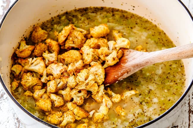 showing how to make cauliflower soup by adding roasted cauliflower to the pot with the broth.
