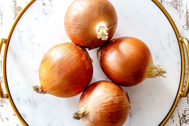 showing yellow onions on a white marble cutting board as the best onions for French Onion Soup