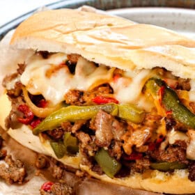 Philly cheese steak on a plate showing the filling oozing with cheese and juicy steak in a hoagie roll