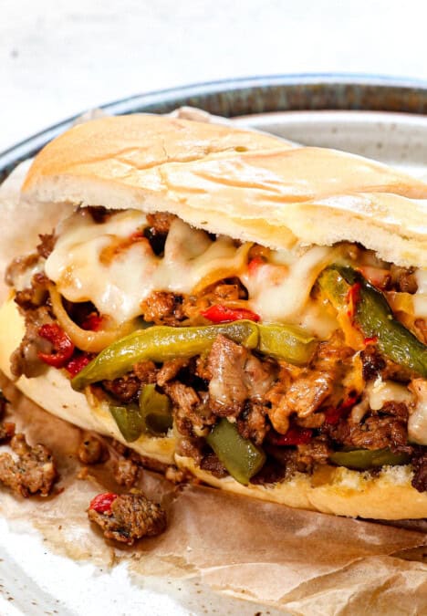 Philly cheese steak on a plate showing the filling oozing with cheese and juicy steak in a hoagie roll