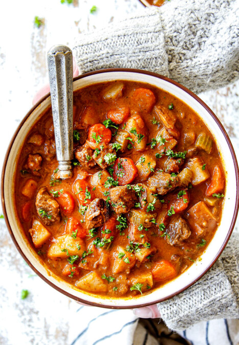 two hands holding a bowl of old fashioned beef stew showing what's in it: beef, potatoes, carrots, celery, onions, garlic, gravy