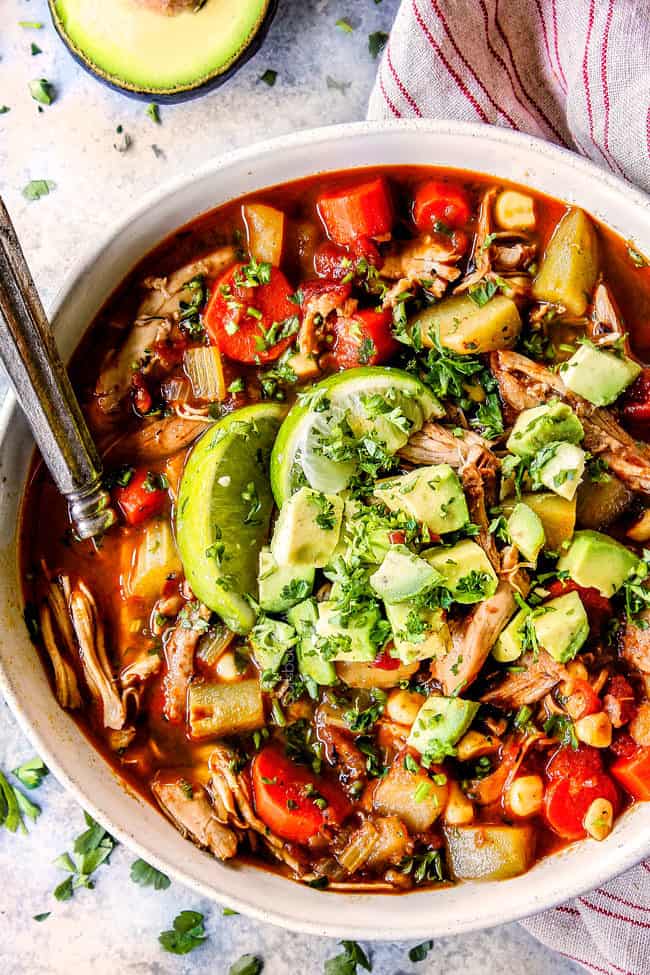 a bowl of authentic Caldo de pollo (Mexican Chicken Soup) toppd with avocadoes, cilantro and limes
