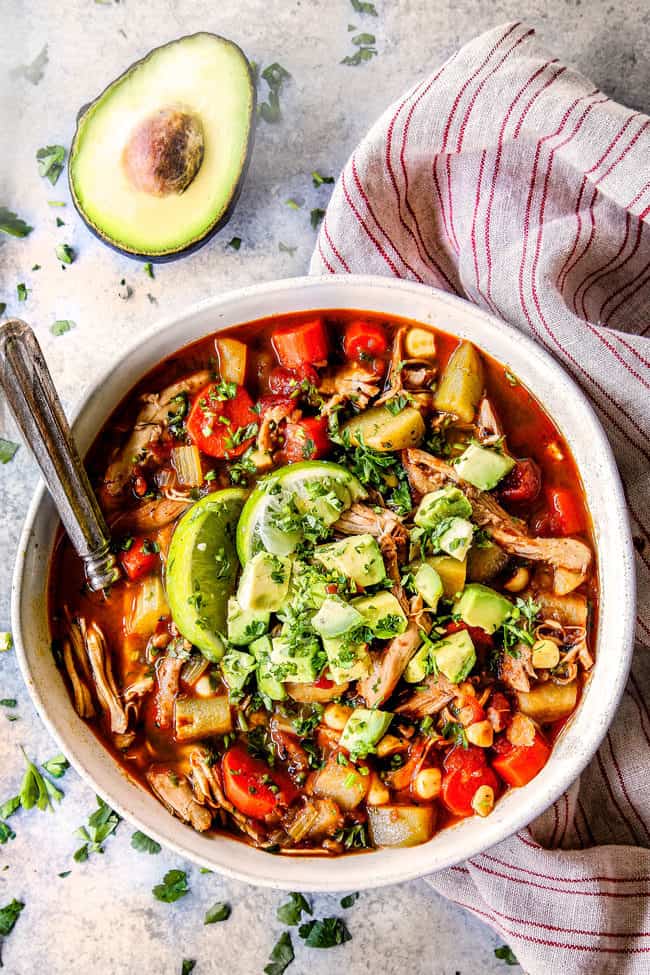 far away top view of best Caldo de pollo (Mexican Chicken Soup) in a white bowl topped with avocados, cilantro and lime juice