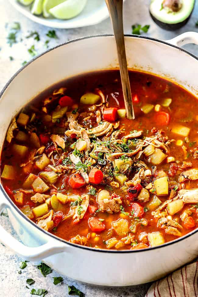 top side view of Caldo de Pollo (Mexican Chicken Soup) in a white pot garnished with cilantro with a copper ladle