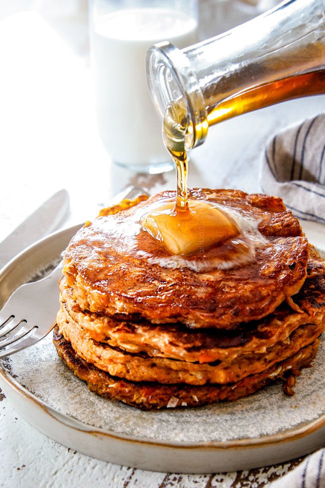 far away shot of pouring syrup over sweet potato pancakes with a slab of butter on top