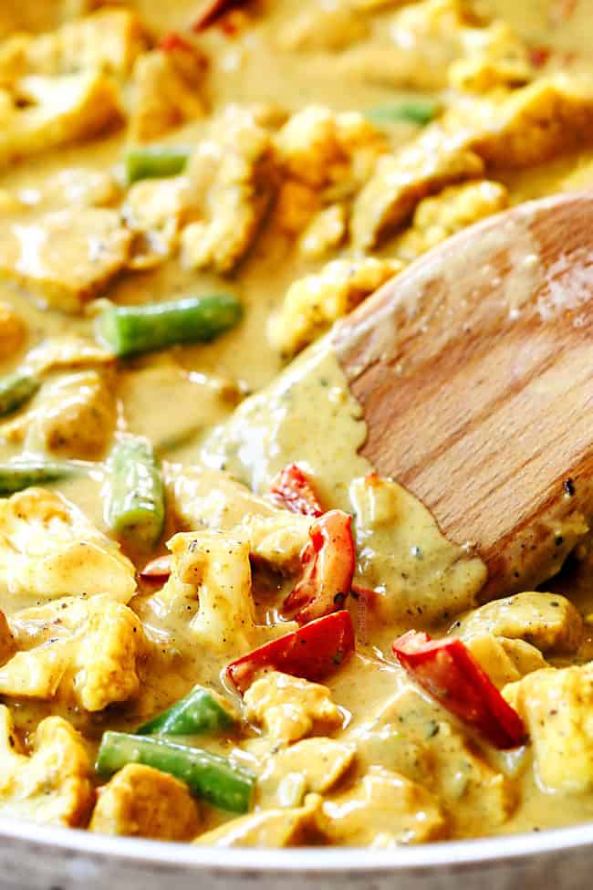 up close of a spoon stirring creamy coconut curry chicken with vegetables