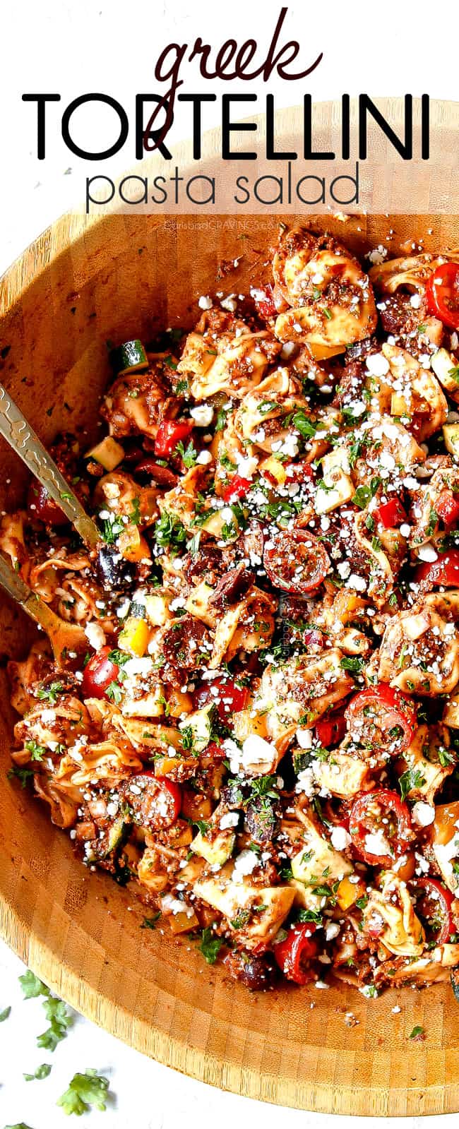 up close top view of best Greek Pasta Salad in a wood bowl with feta, tomatoes, olives, cucumbers, spinach