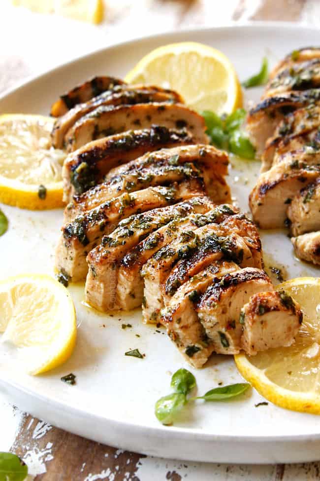 marinated lemon basil chicken on a white plate with lemon slices and basil