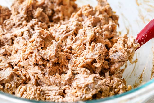 showing how to make chicken enchiladas by mixing chicken, sour cream, green enchilada sauce and cheese together in a white bowl.