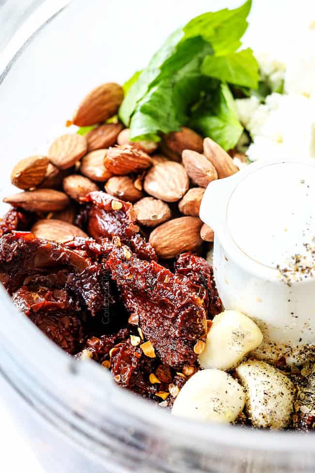 showing how to make Greek Salad Dressing by adding red wine vinegar, sun dried tomatoes, lemon juice, oregano, red pepper flakes to food processor