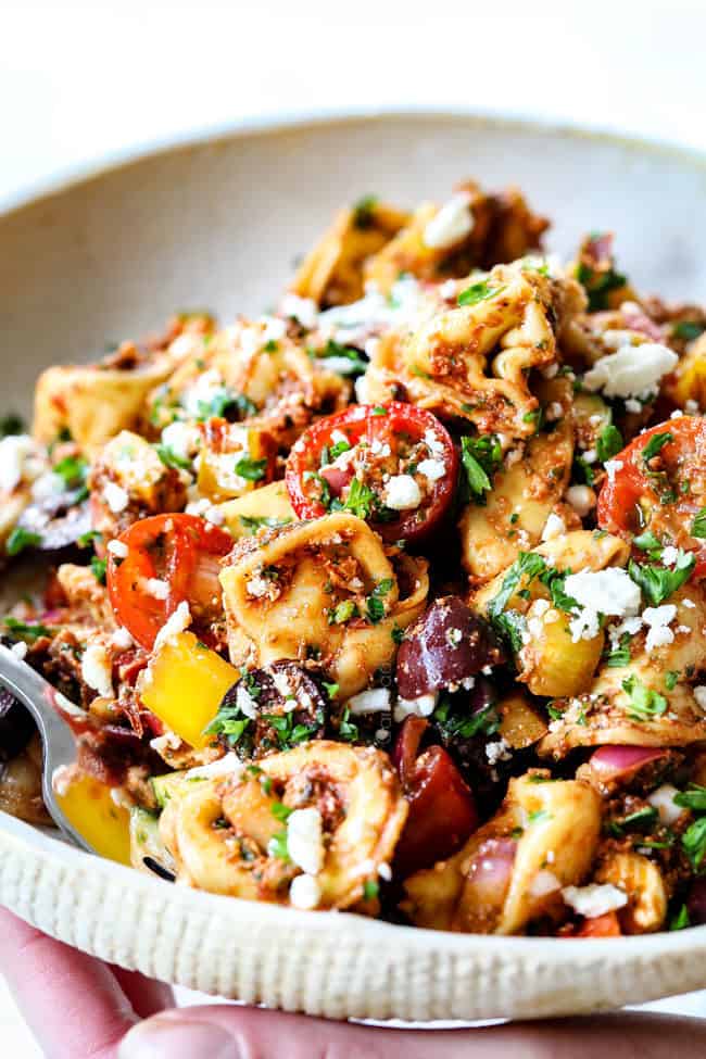 side view of greek pasta salad with feta and spinach on a white plate with a fork in it