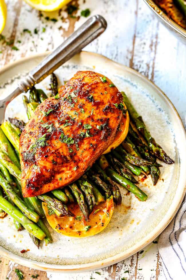 top view of a piece of lemon pepper chicken and asparagus on a plate garnished by lemons with a fork