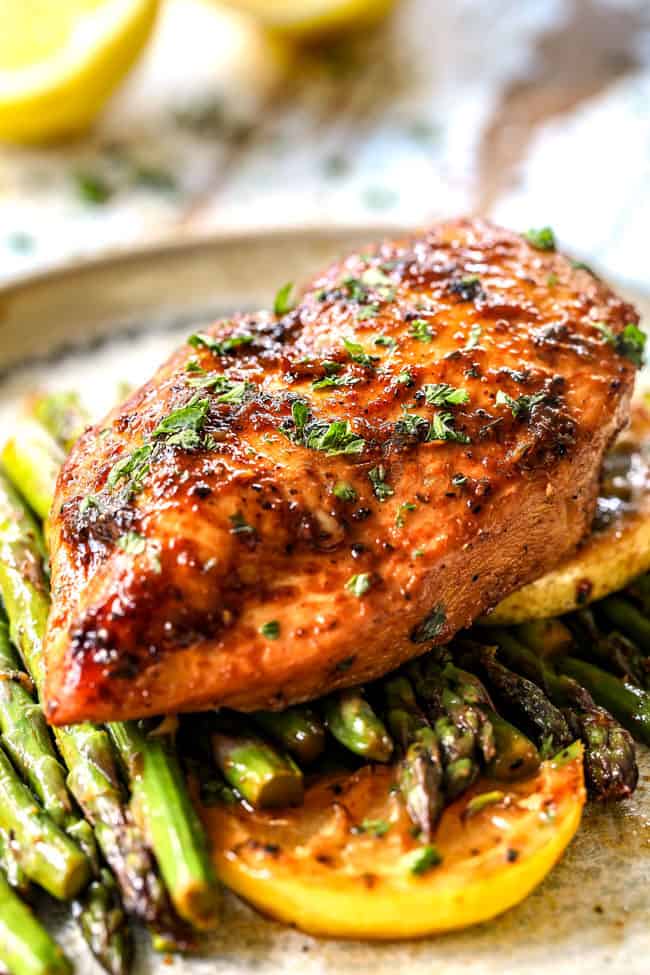 up close of a piece of lemon pepper chicken and asparagus on a plate garnished by lemons