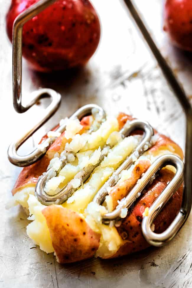 showing how to make smashed potatoes by smashing red potatoes with a potato masher