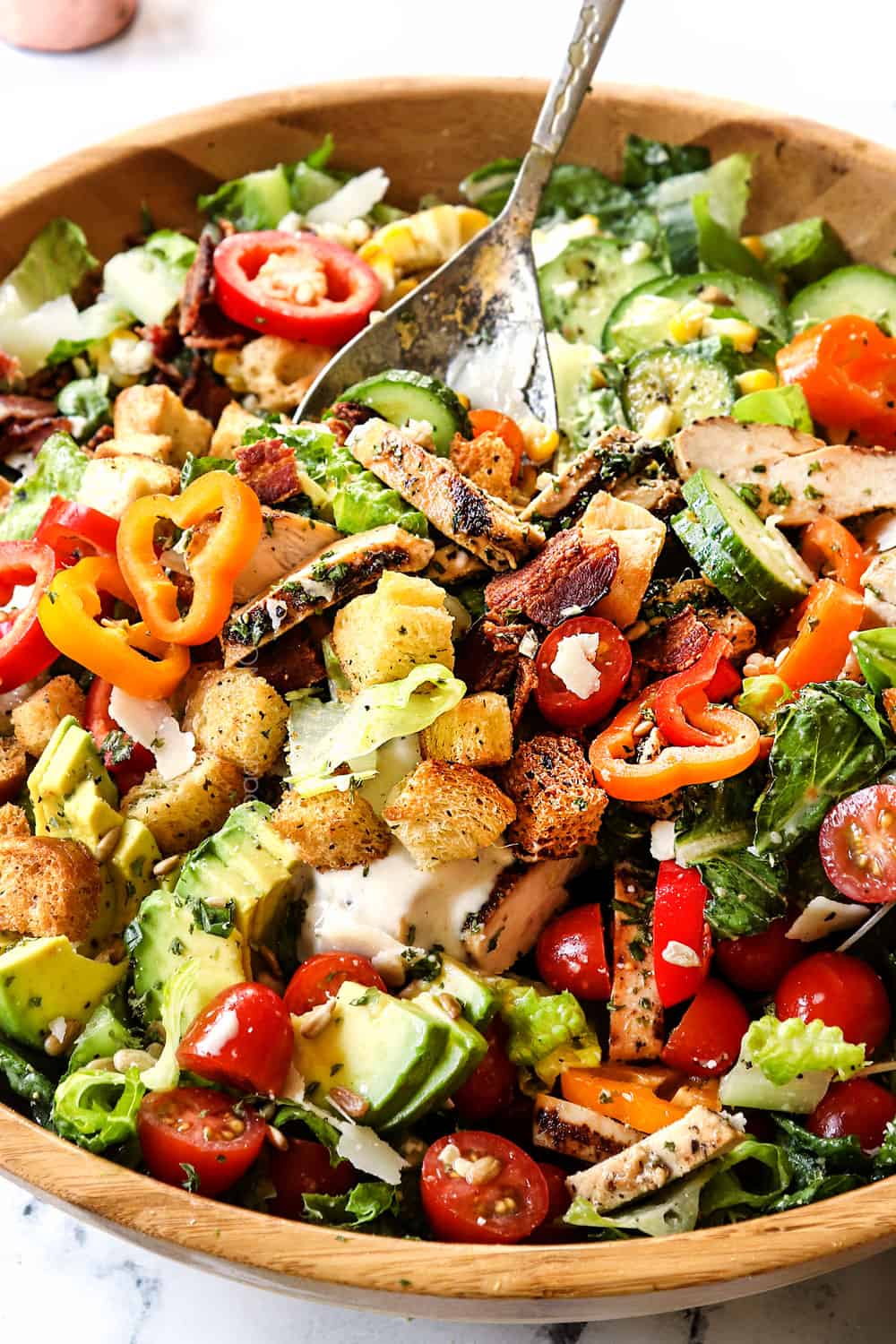showing how to serve Chicken Caesar Salad with grilled chicken by tossing all of the ingredients together in a bowl with tongs