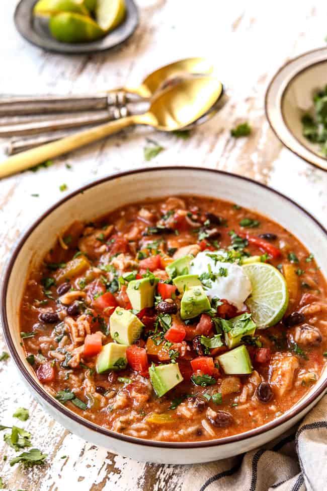 showing how to garnish chicken fajita soup by topping a bowl of soup with tomatoes, avocados, cilantro and sour cream