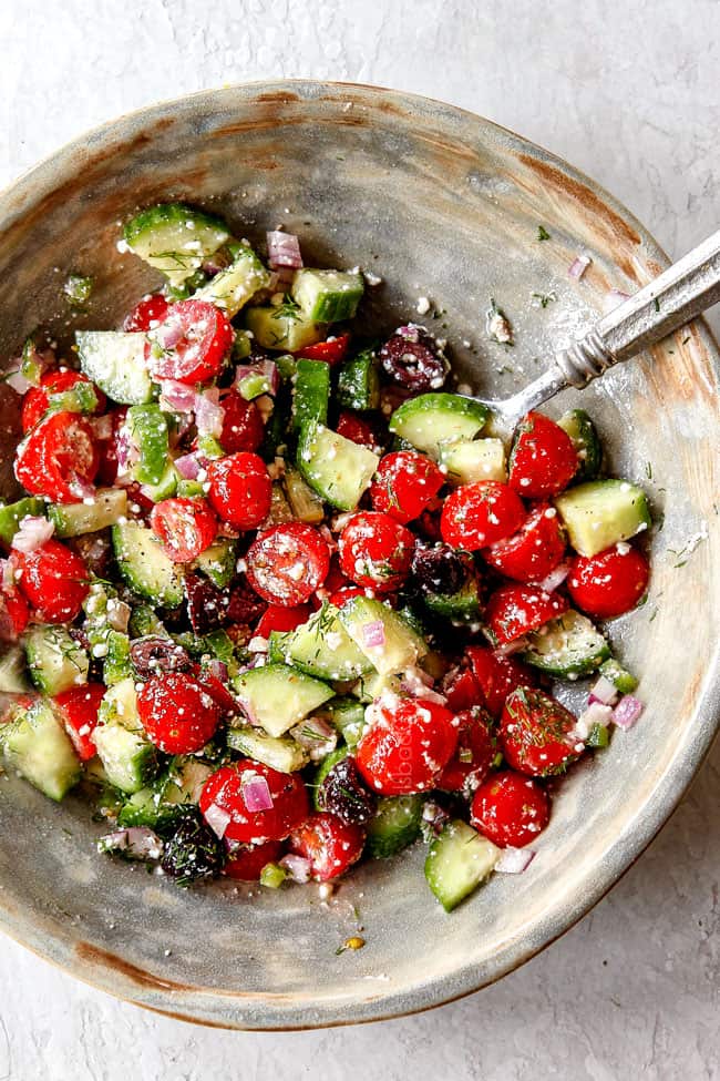 top view showing how to make salad for Greek chicken by tossing cucumbers, dill and tomatoes together in a bowl