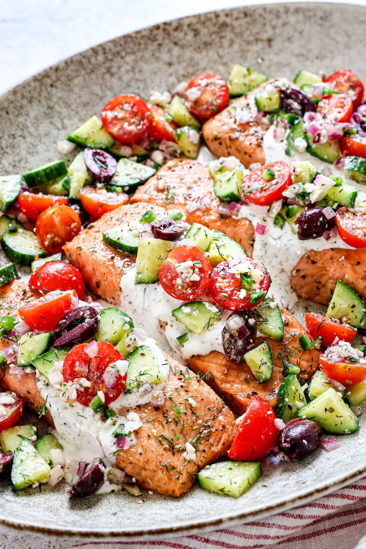 Side view of dill sauce salmon recipe on a platter garnished by tomatoes and cucumbers