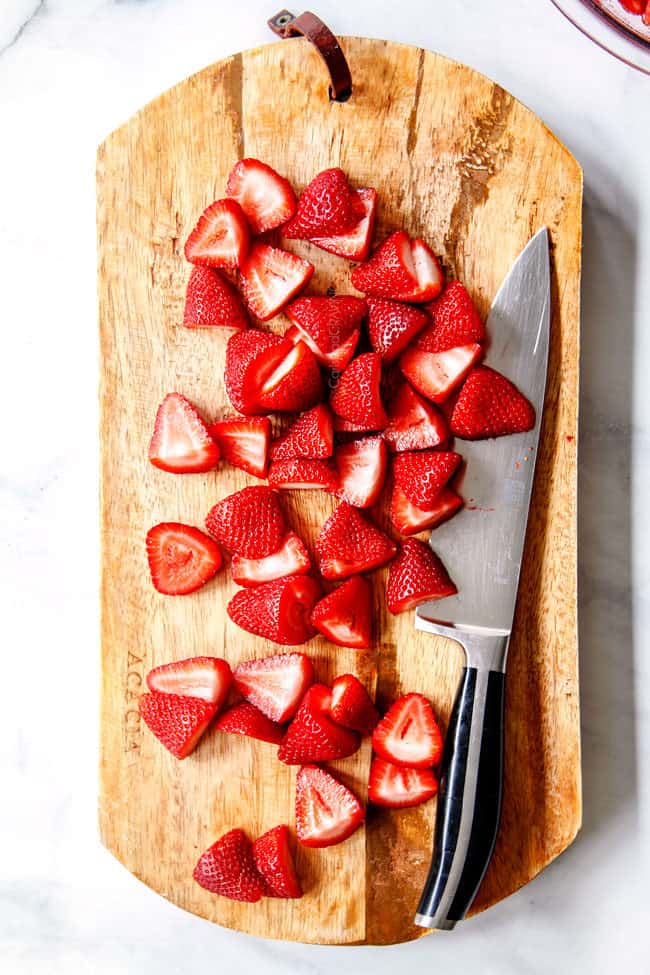 showing how to make strawberry shortcake cake by slicing strawberries in half o a cutting board