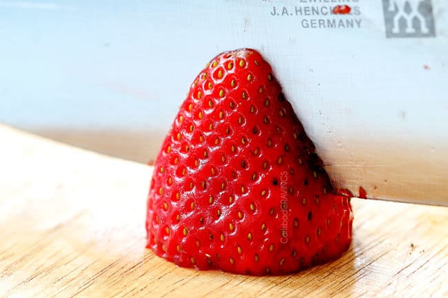showing how to make strawberry shortcake cake by slicing strawberries in half for filling