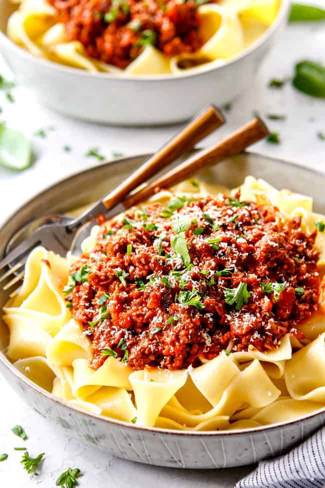 showing how to serve best Bolognese recipe by adding sauce to pasta and topping with freshly grated Parmesan