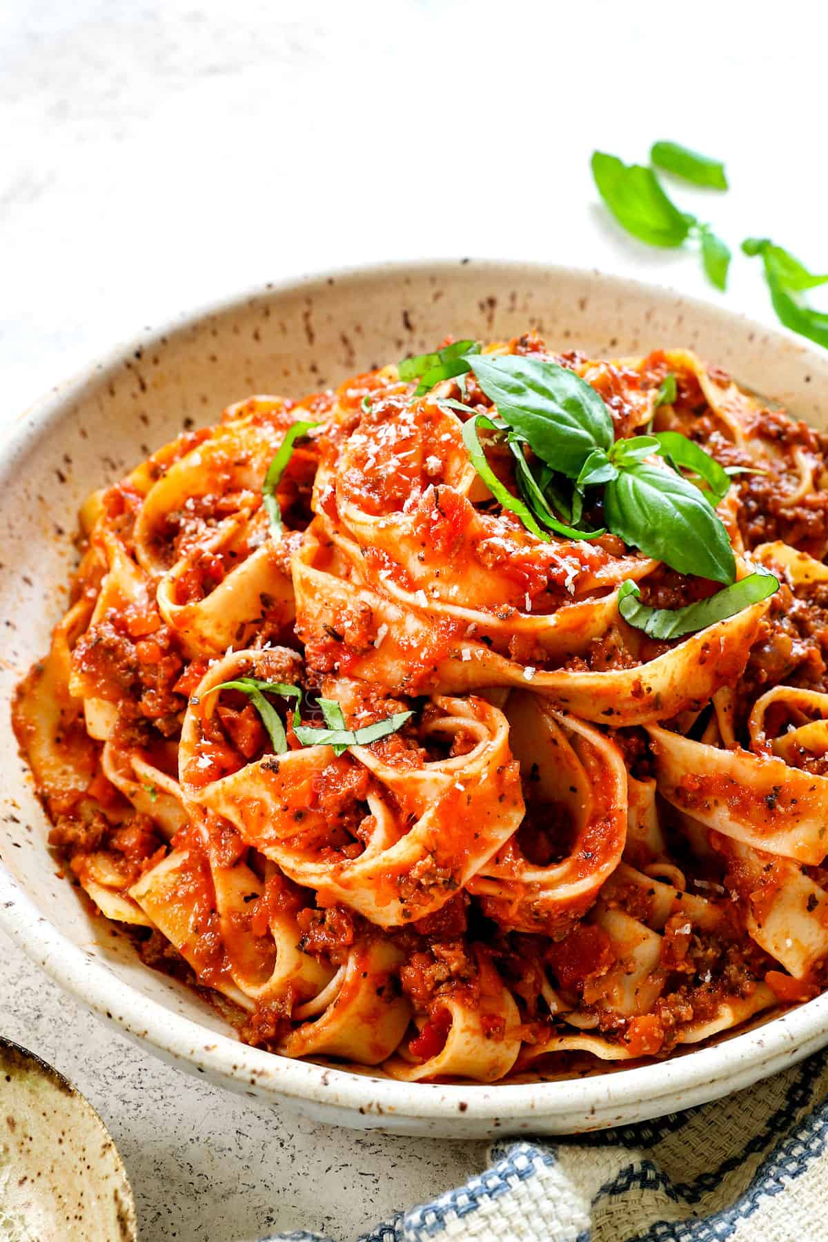 serving Bolognese with pasta in a bowl garnished with basil and Parmesan