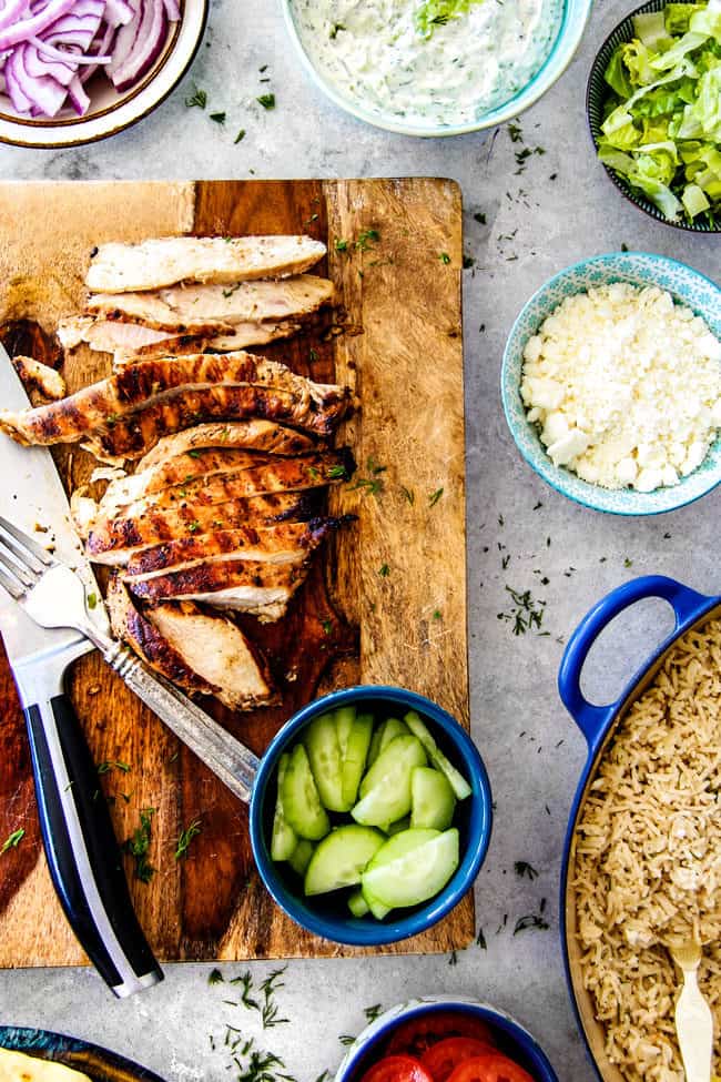 showing how to make Greek chicken gyro recipe with top view of red onions, lettuce, feta, cucumbers, tomatoes, tzatziki