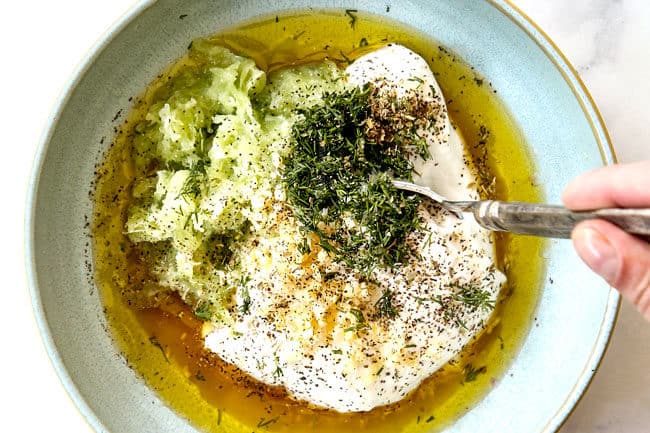 showing how to make Tzatziki by stirring Greek yogurt, cucumbers, dill, garlic, vinegar and olive oil in a bowl