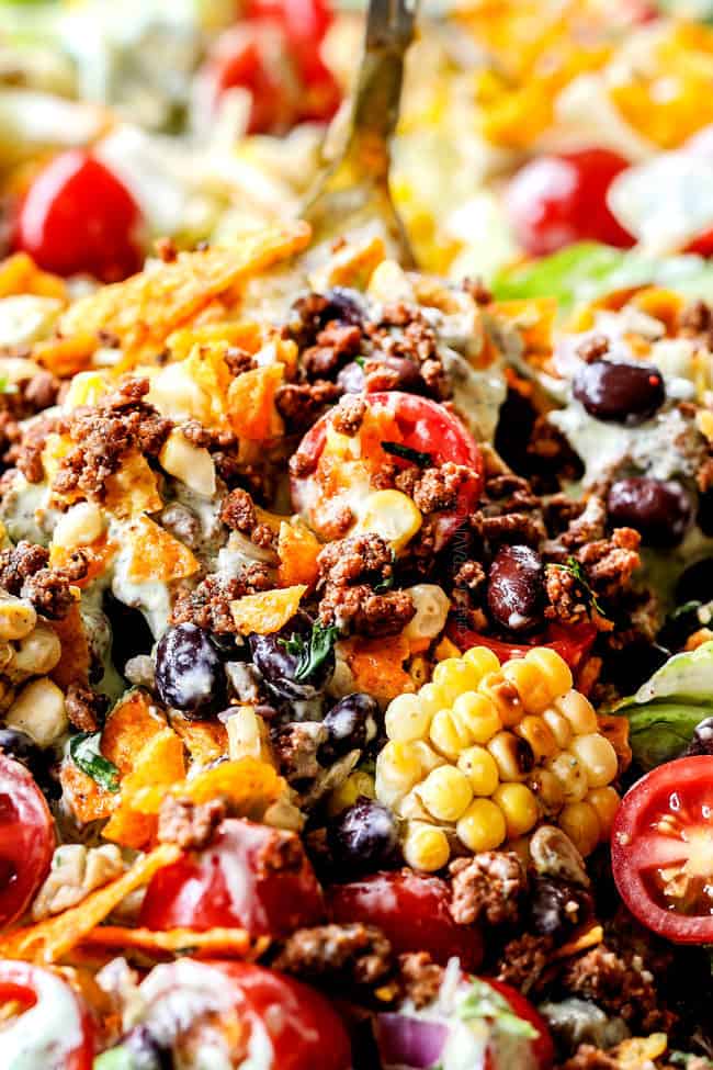 up close showing how to make taco salad by tossing salad with taco salad dressing