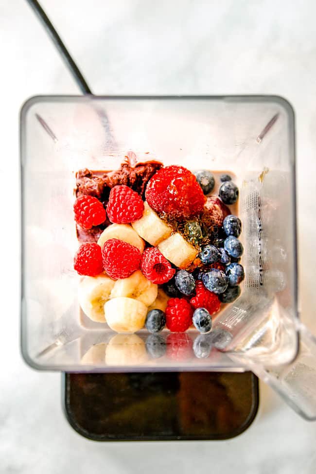 showing how to make berry acai bowls by adding bananas, strawberries, blueberries and milk to blender