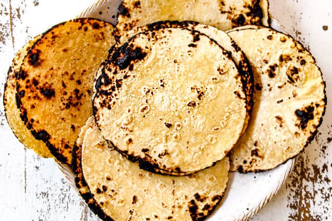 showing how to make flank steak tacos by warming corn tortillas